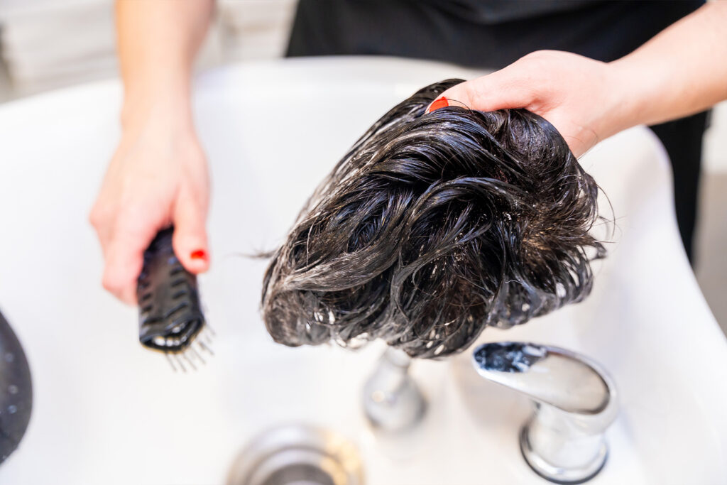 Une femme qui nettoie et brosse une perruque de cheveux naturels bruns